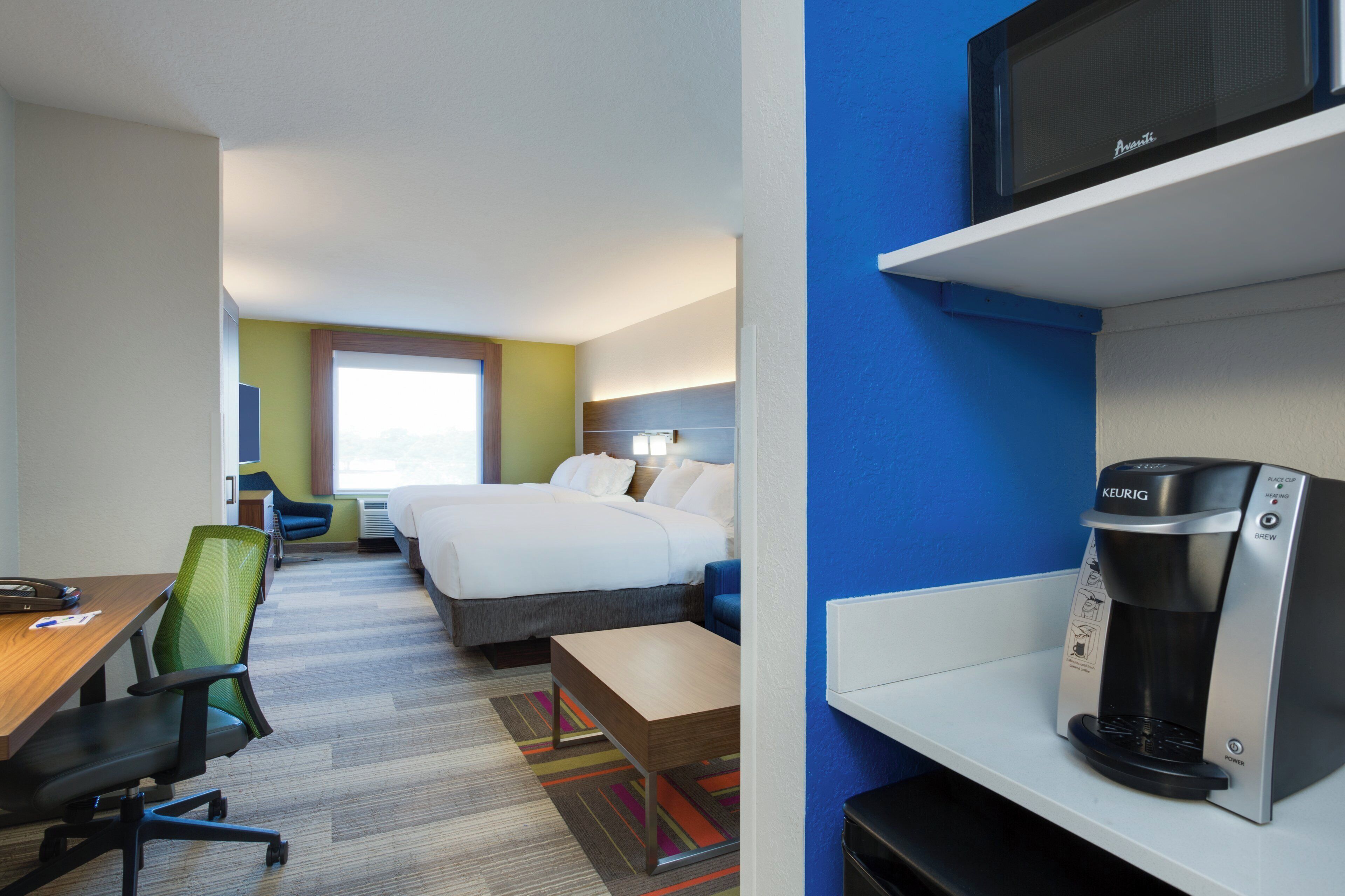 A hotel room with a bed, a desk with a chair, a microwave, and a coffee maker.