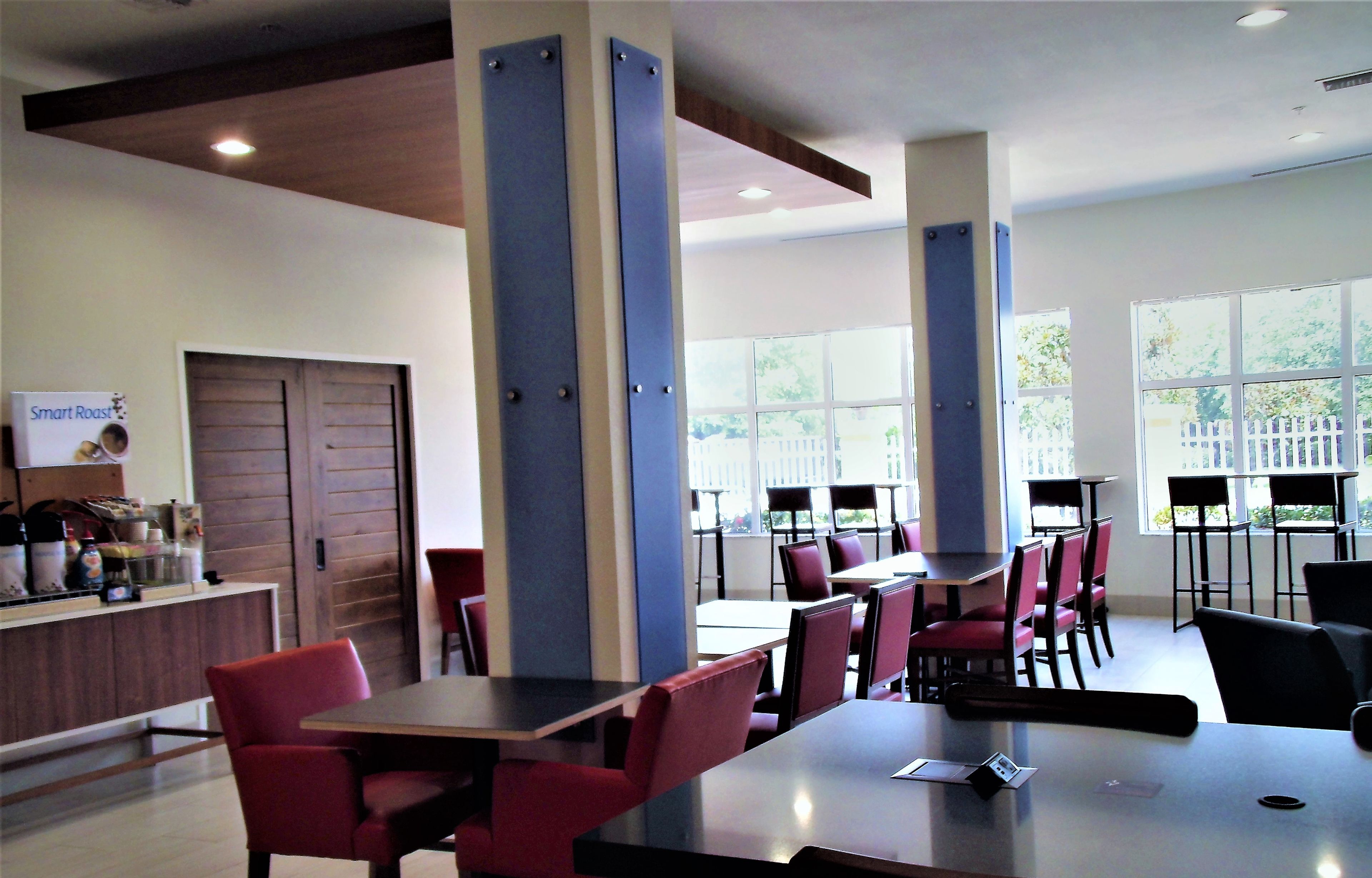 A restaurant with high tables and red chairs, large windows, and a wooden door.