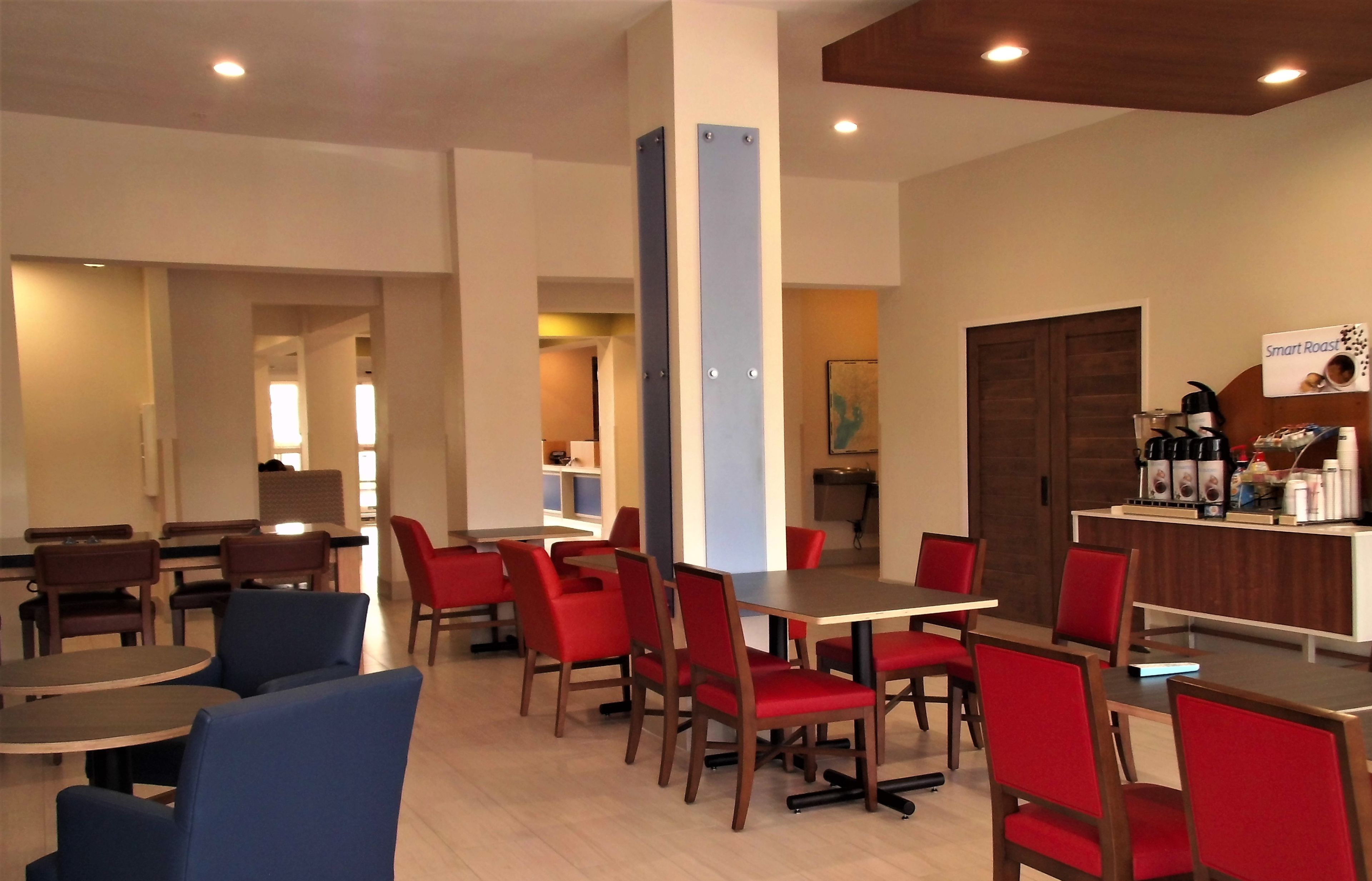 A modern dining area with red and blue chairs, wooden tables, and a counter with a sign reading "Smart Roast".