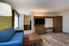 Ein gemütlicher, kompakter Wohnraum mit einer Couch, einem kleinen Tisch, einem Fernseher und einer Küchenzeile im Hintergrund.