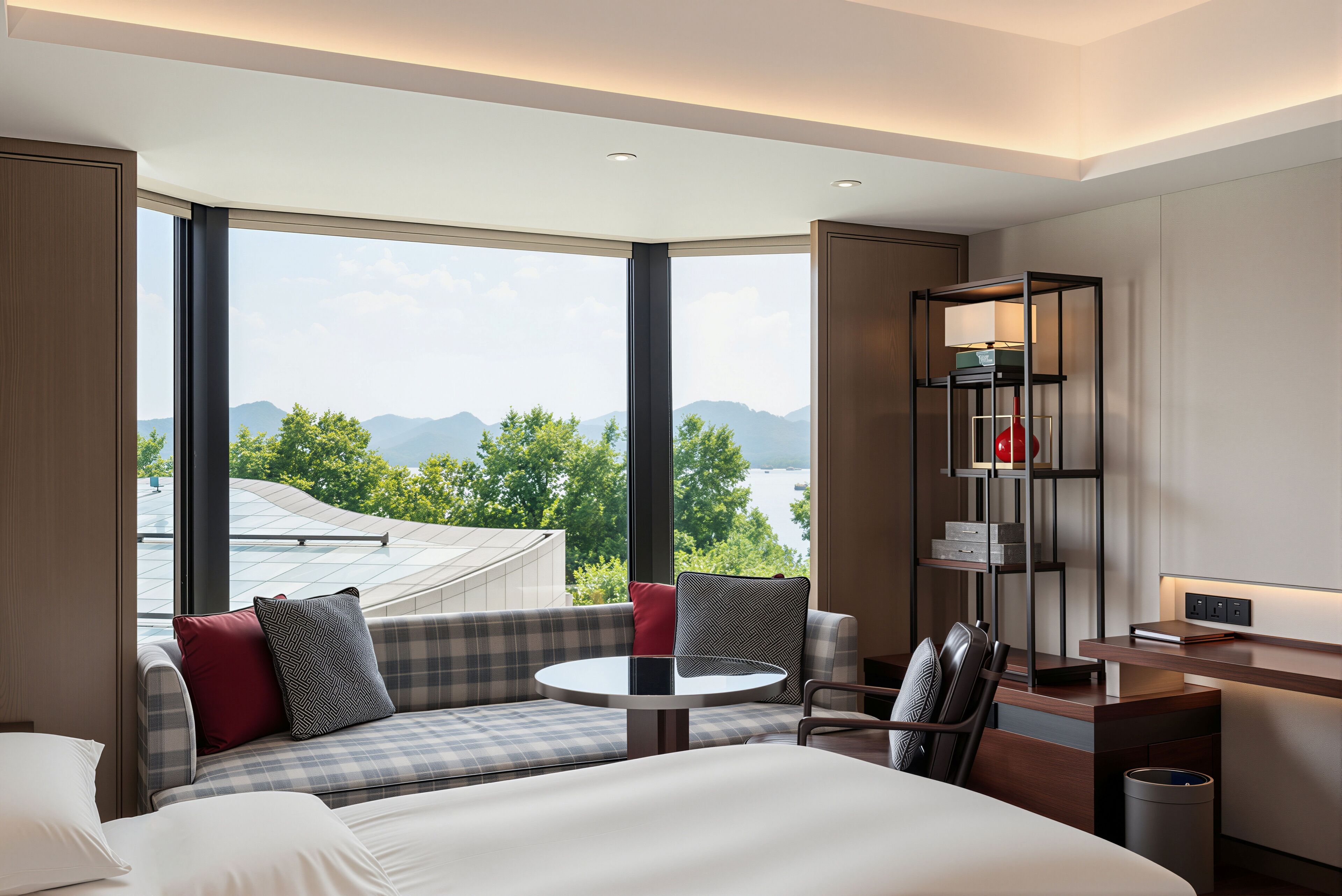 Habitación de hotel moderna con un ventanal grande, una cama, una zona de estar con una mesa y un escritorio con una lámpara.