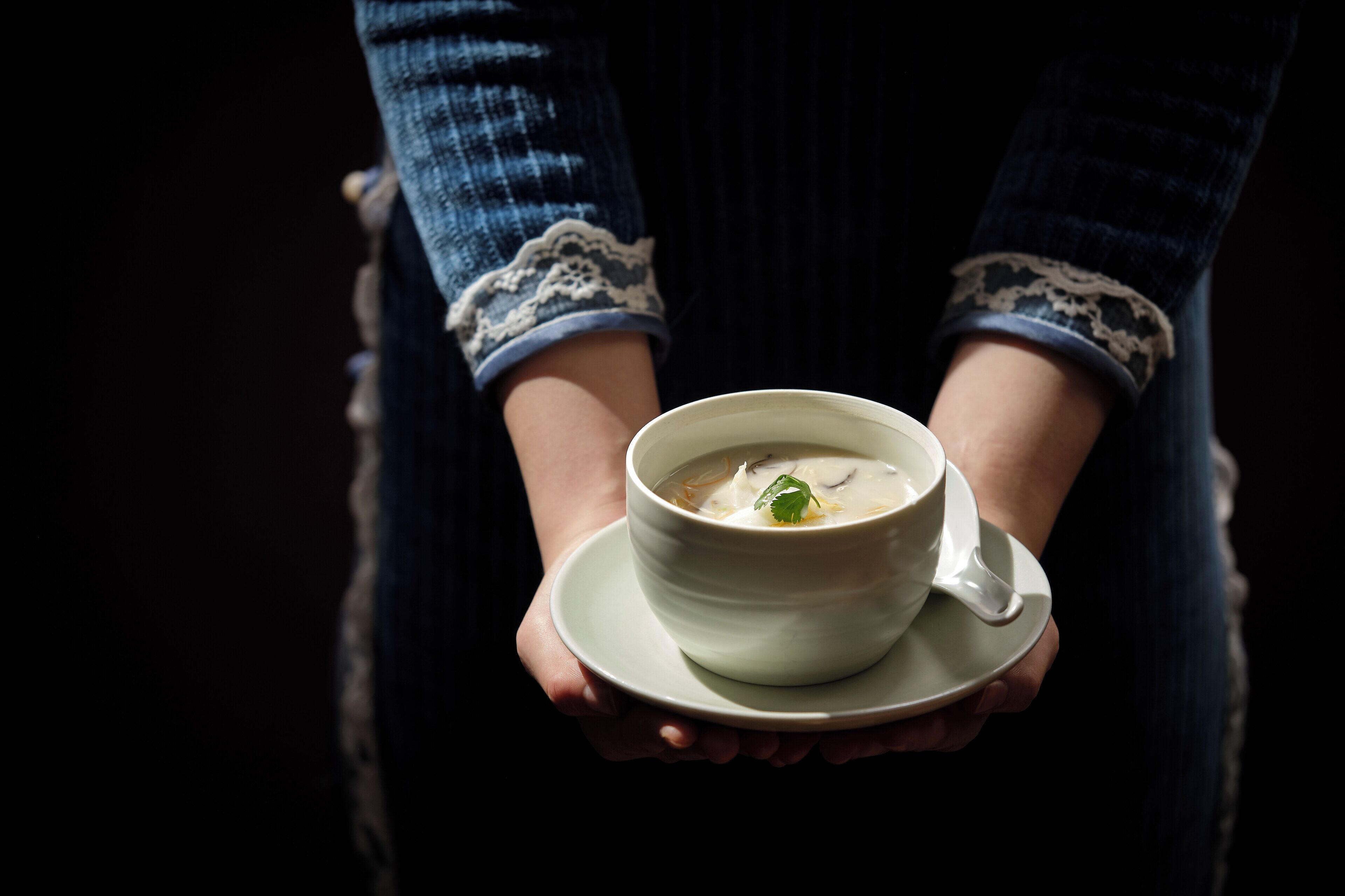 Eine Person hält eine Schüssel Suppe mit einem Löffel auf einem Untertaler.