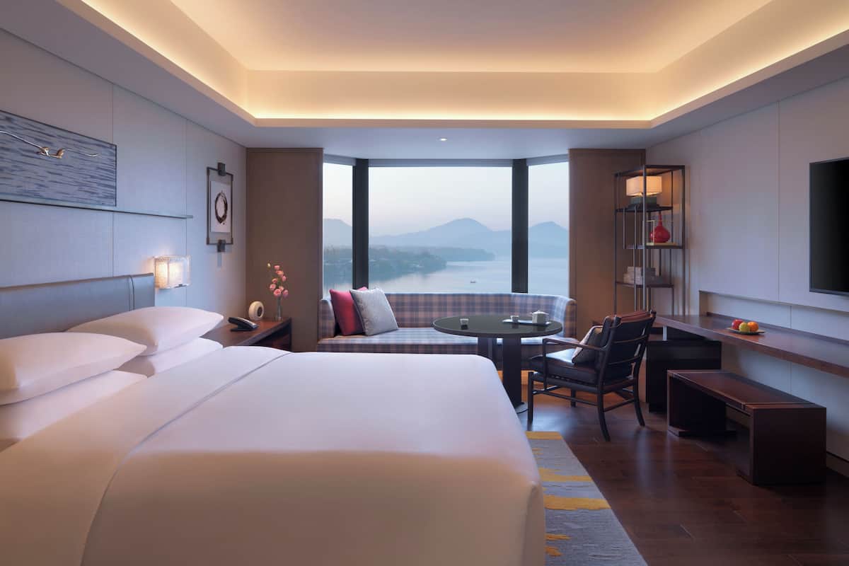 A hotel room with a large bed, a seating area with a table, and a view of mountains through large windows.