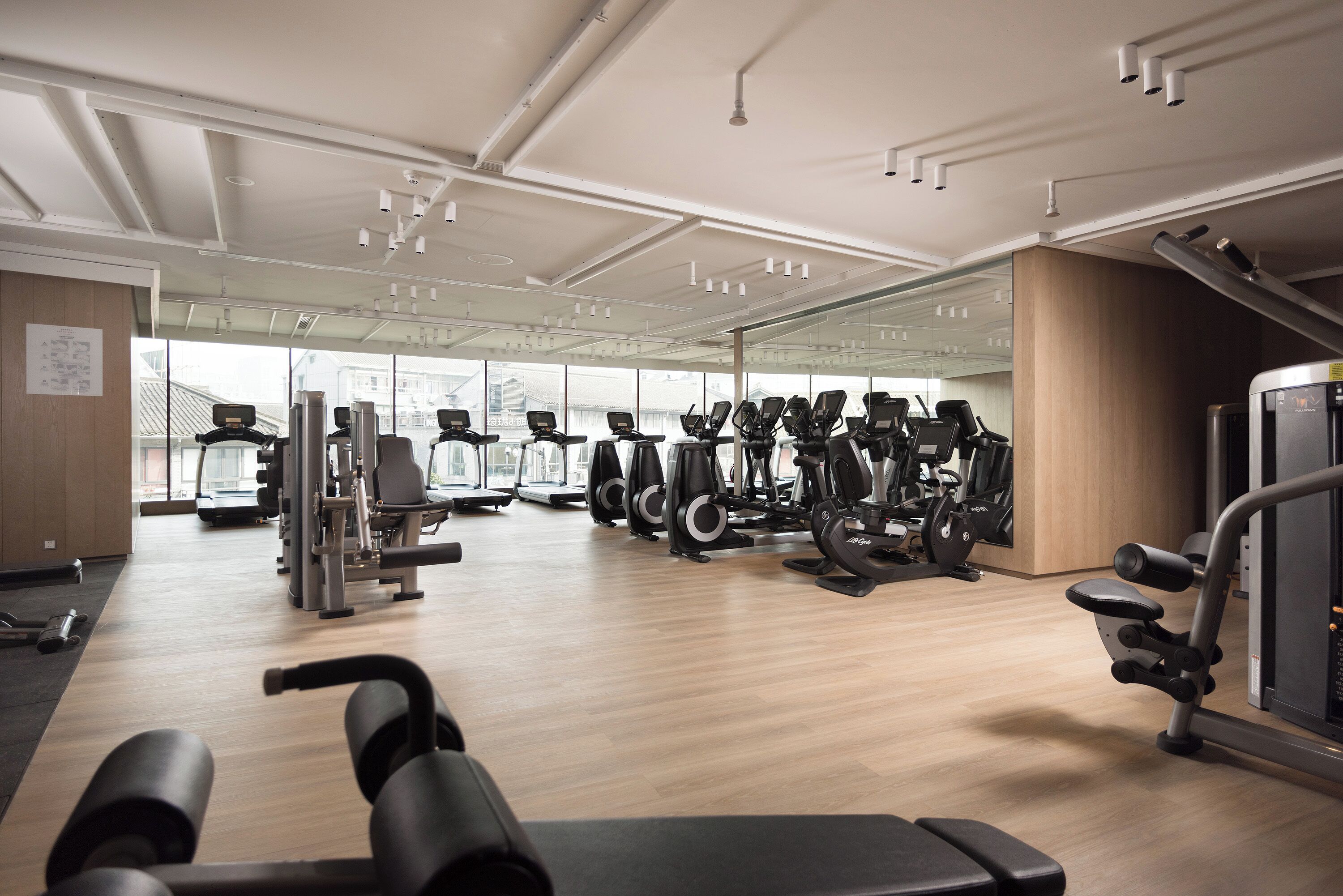 Ein Fitnessstudio mit unterschiedlichen Trainingsgeräten, großen Fenstern und einem Holzboden.