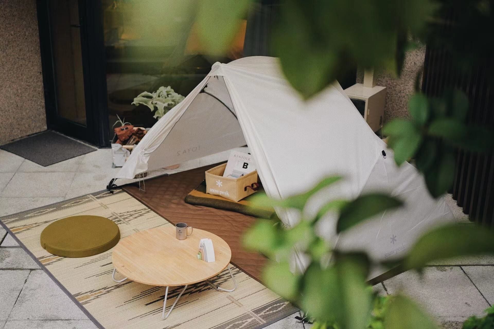 A tent set up on a tiled patio with a round wooden table, a small stool, and a box of tissues.