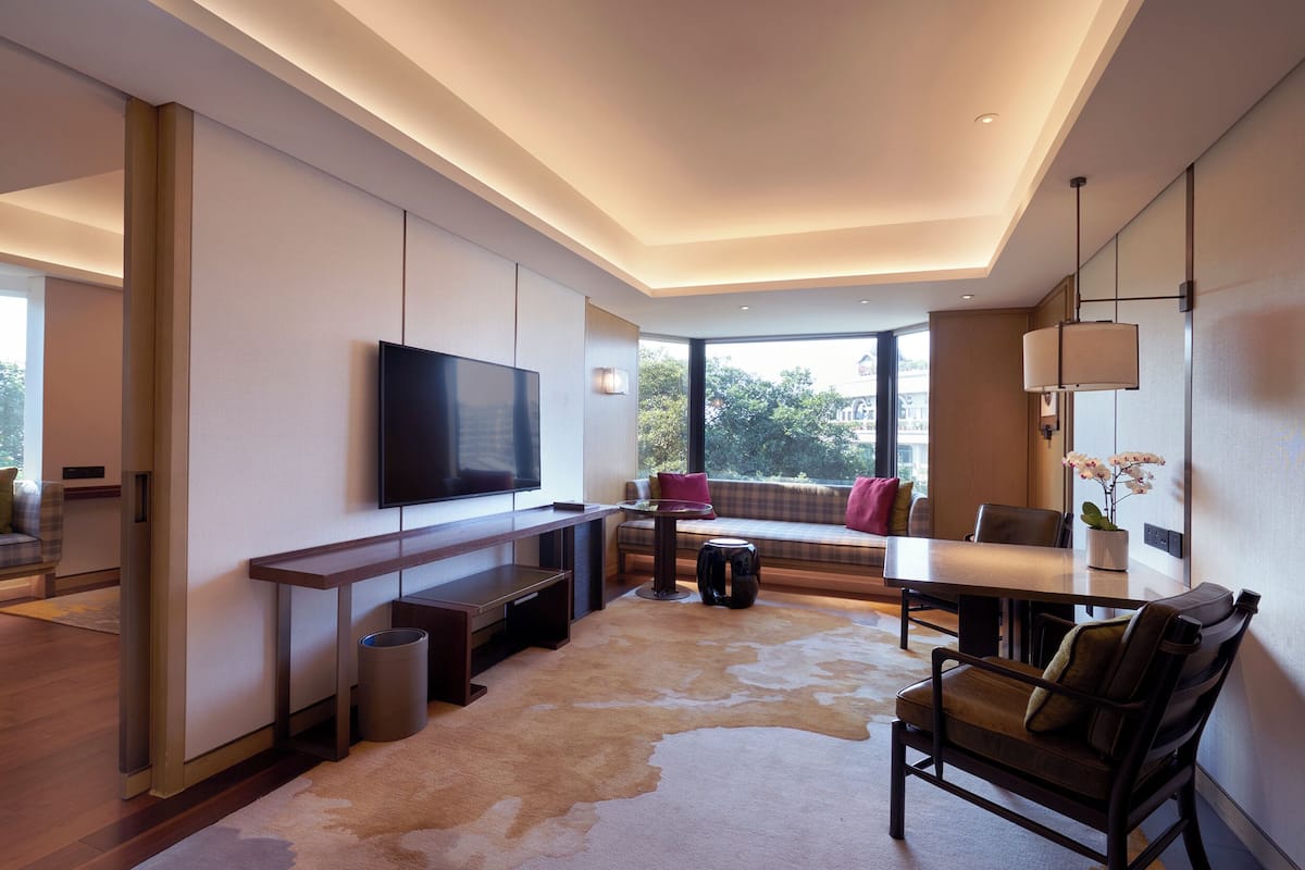A modern living room with a flat-screen TV, a dining area, and a large window offering a view of the outdoors.