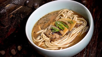 A bowl of noodle soup with a meat topping and green garnish, placed on a wooden surface.