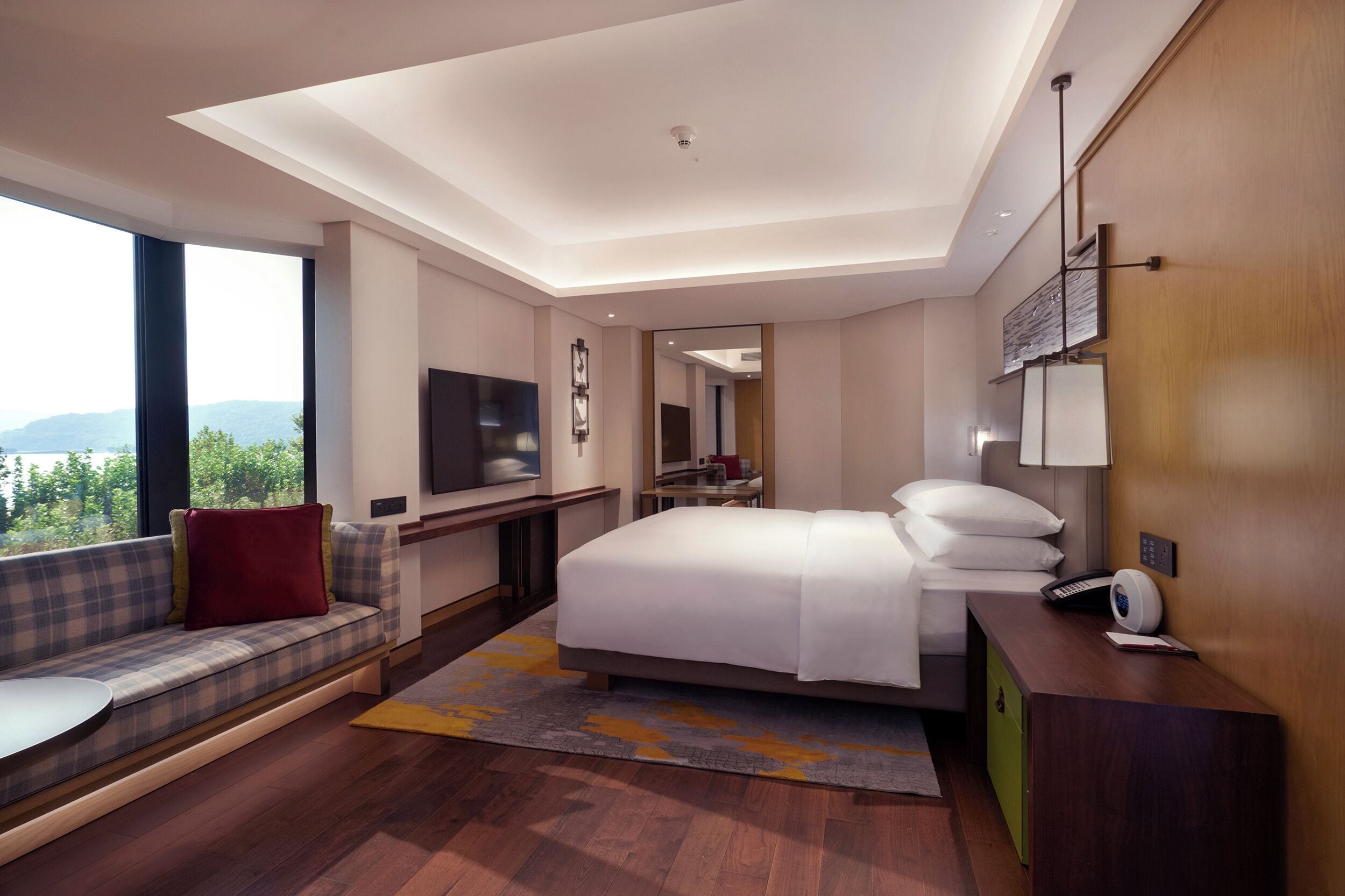 A modern hotel room with a large bed, a seating area with a view, a flat-screen TV, and a desk with a lamp.