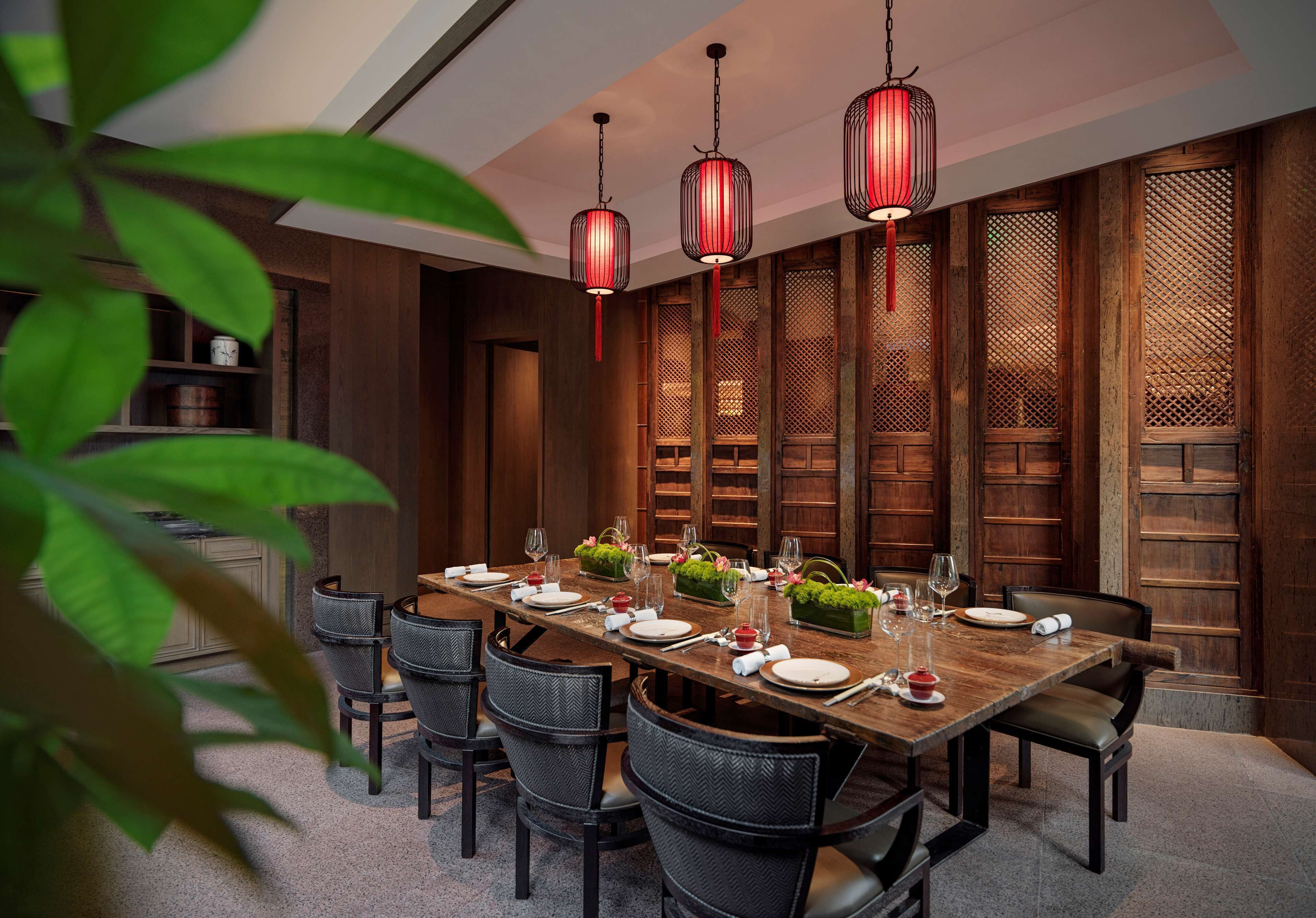 A dining area with a long wooden table set for six, surrounded by dark chairs. There are three hanging red lanterns above the table.