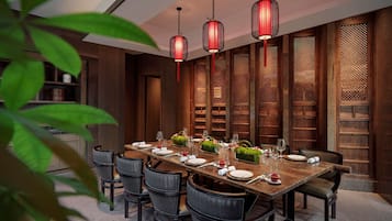 Un comedor con una larga mesa de madera dispuesta para seis personas, rodeada de sillas oscuras. Tres faroles rojos cuelgan sobre la mesa.
