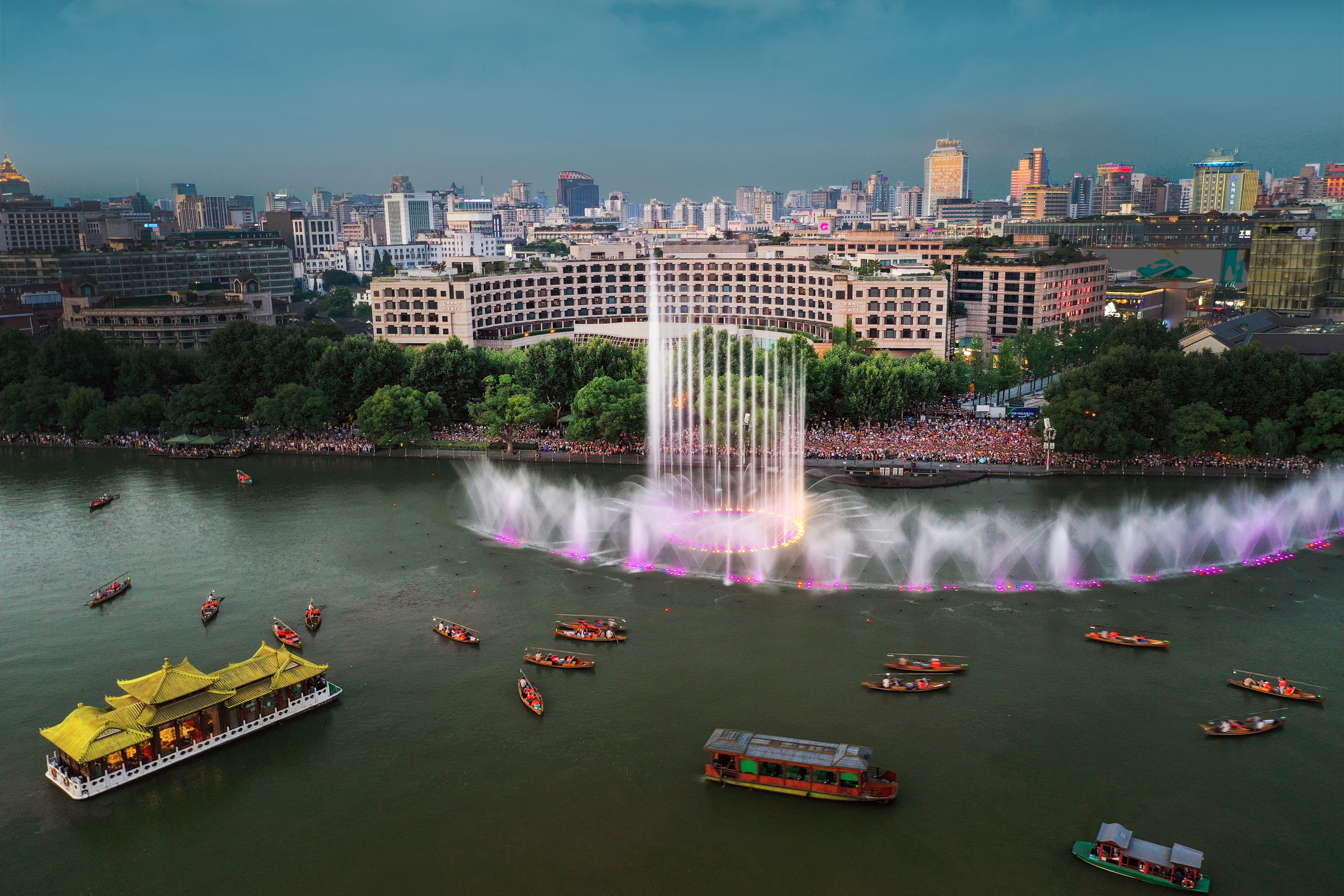 A cityscape with a prominent building in the background, a large fountain in the foreground, and several boats on the water.