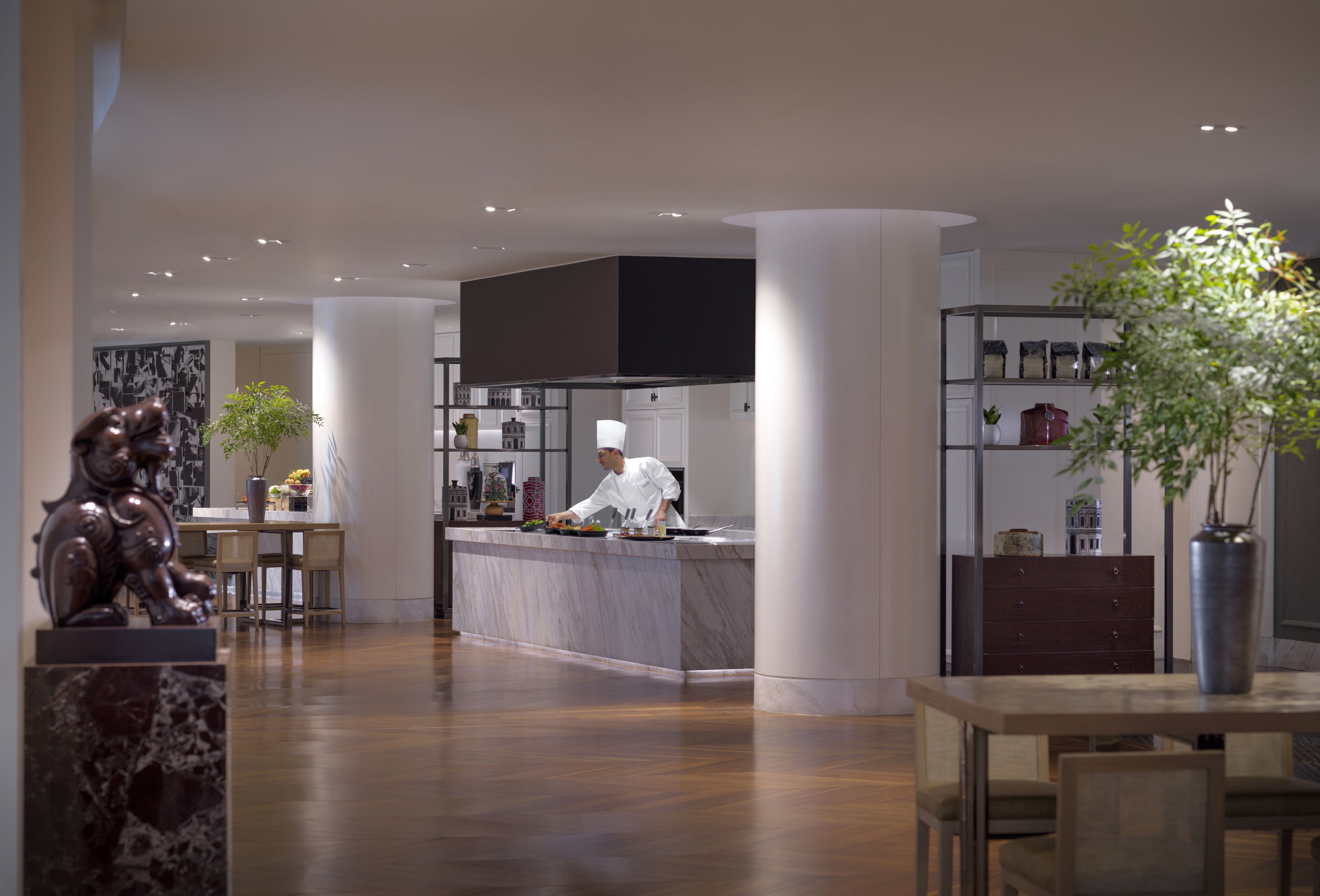 Een moderne keuken met een kok die kookt, een eethoek met een tafel en stoelen, en een decoratief beeld.