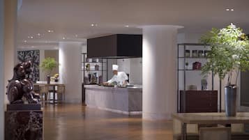 A modern kitchen with a chef preparing food, a dining area with a table and chairs, and a decorative statue.
