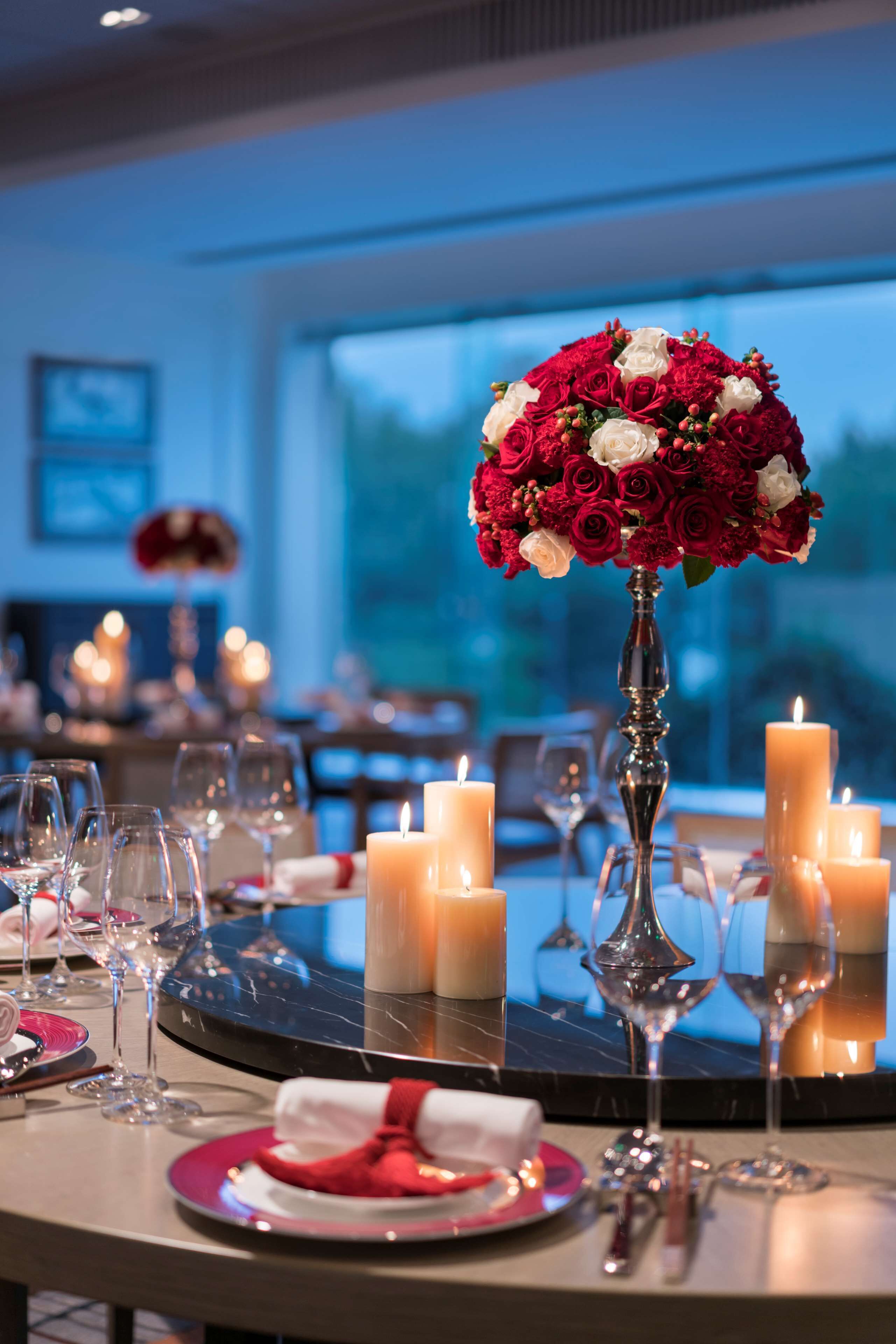 A dining table set with candles, wine glasses, and a centerpiece of red and white flowers.