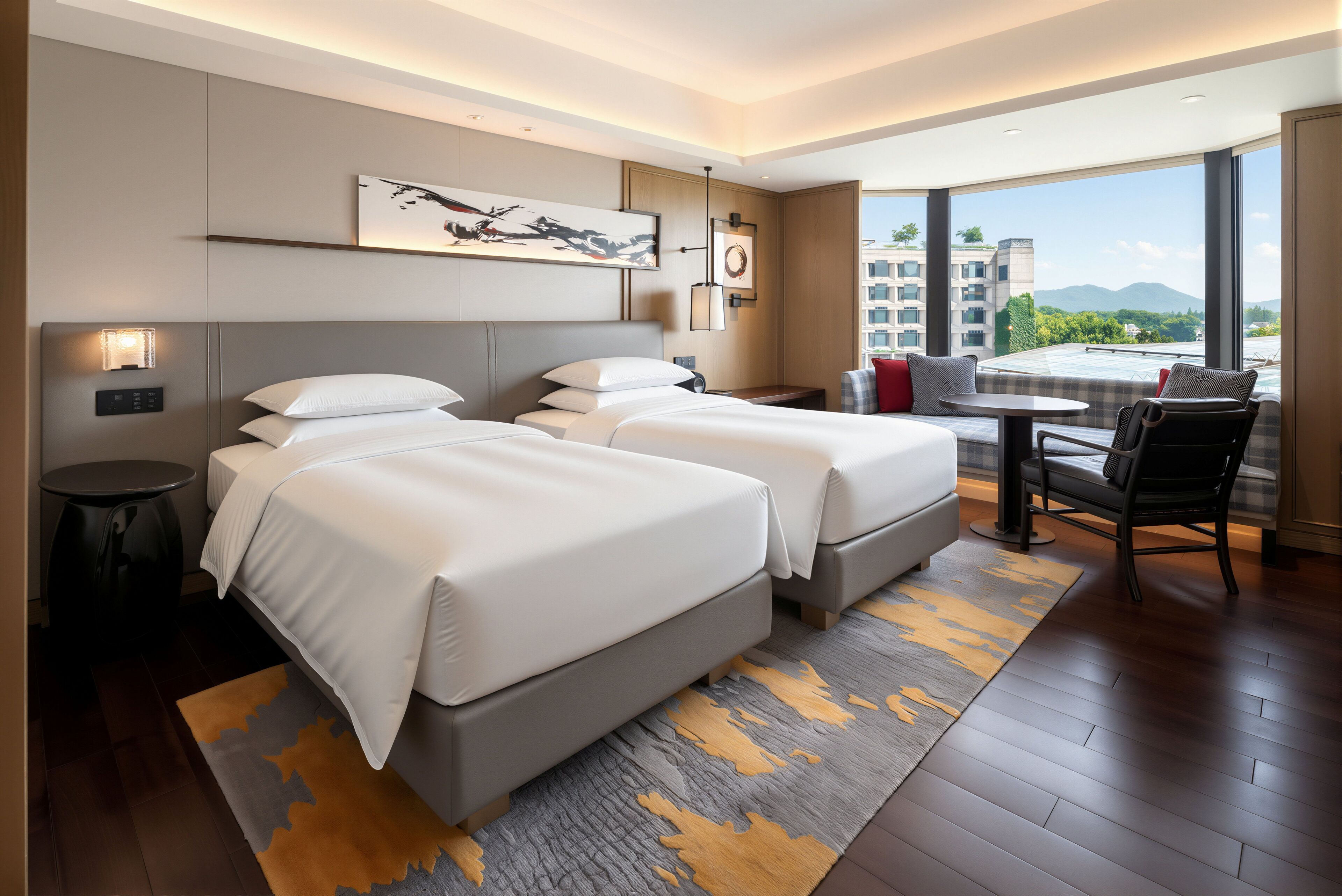 A hotel room with two beds, a small table, a chair, and a view of the cityscape.