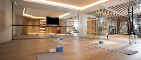 A modern gym with wooden floors, exercise mats, and a large mirror.