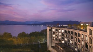 Un hotel moderno con vista a un lago y montañas al anochecer.