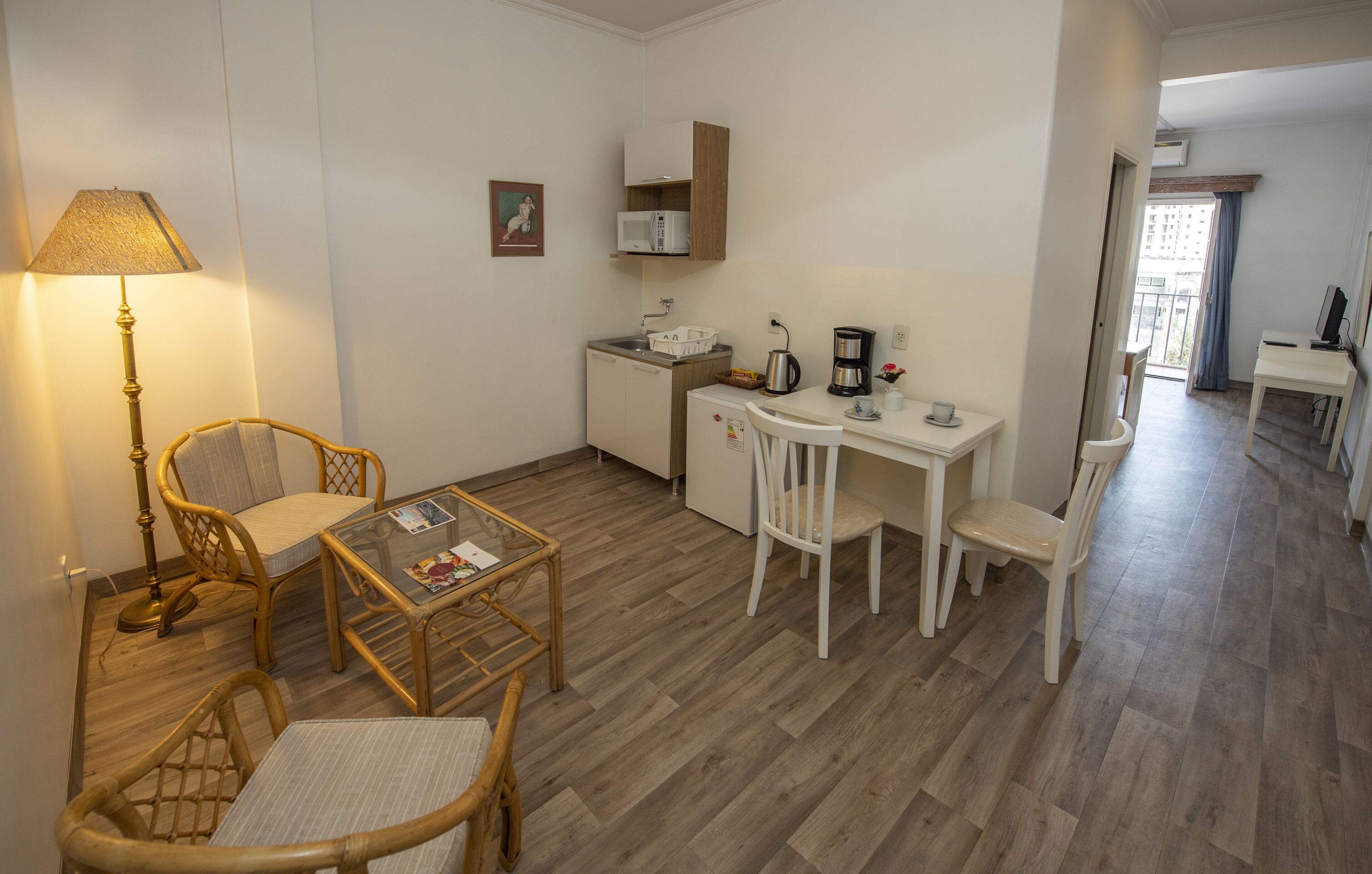 Een compacte woonruimte met een kitchenette, een eethoek en een zithoek met een lamp en een stoel.