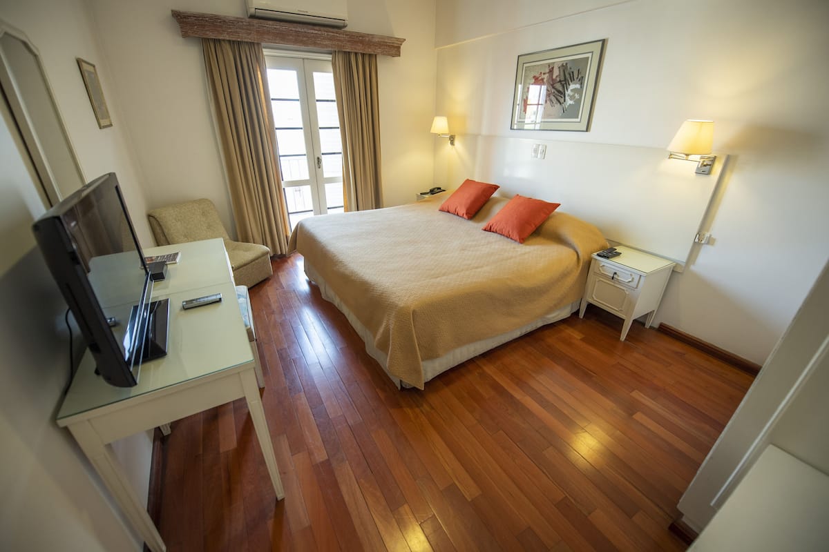 A hotel room with a bed, bedside tables, a desk with a computer, a chair, and a window with curtains.
