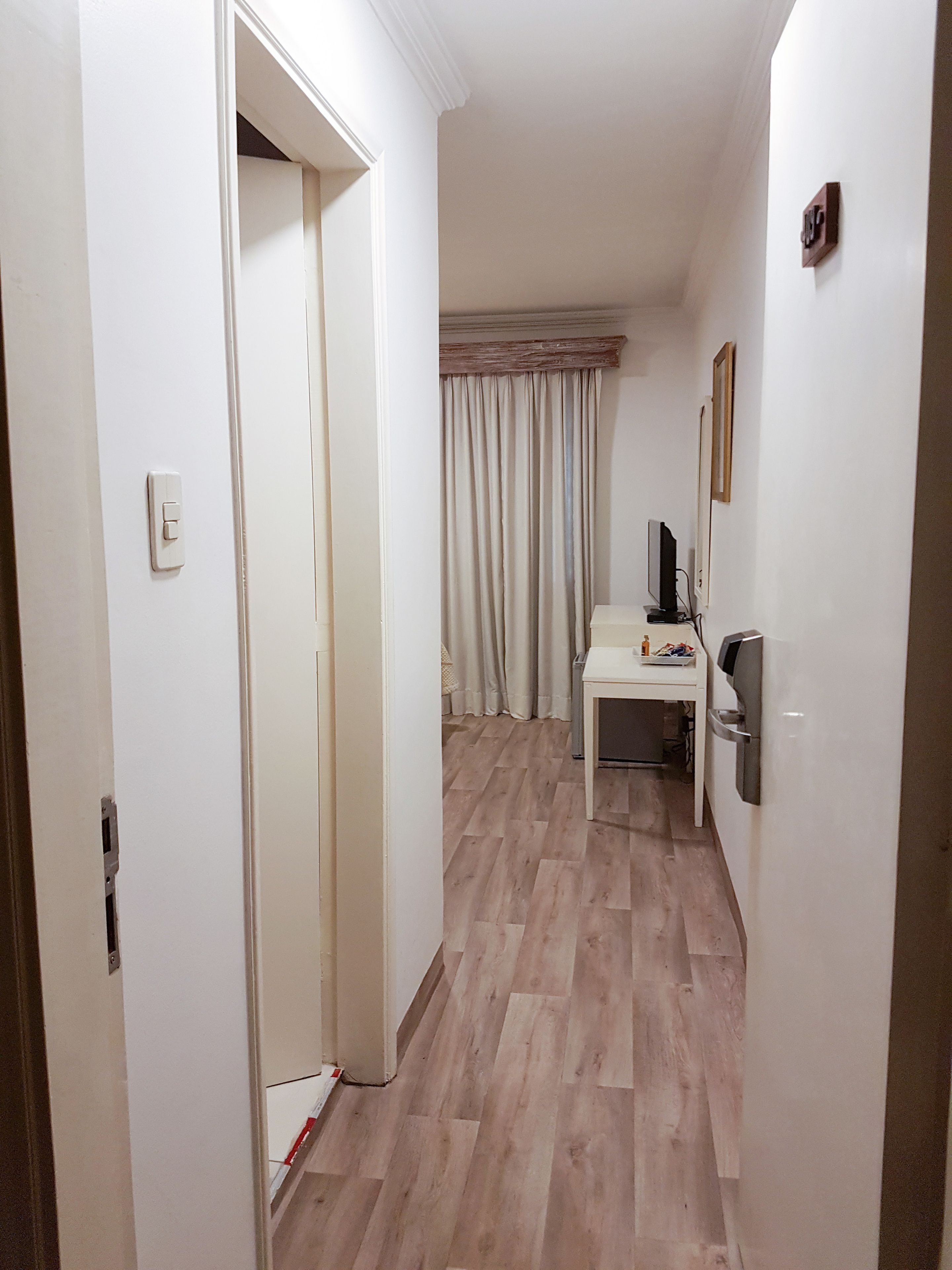 Ein Gang mit Holzboden, einer weißen Tür, einer weißen Wand und einem Fenster mit Vorhängen.