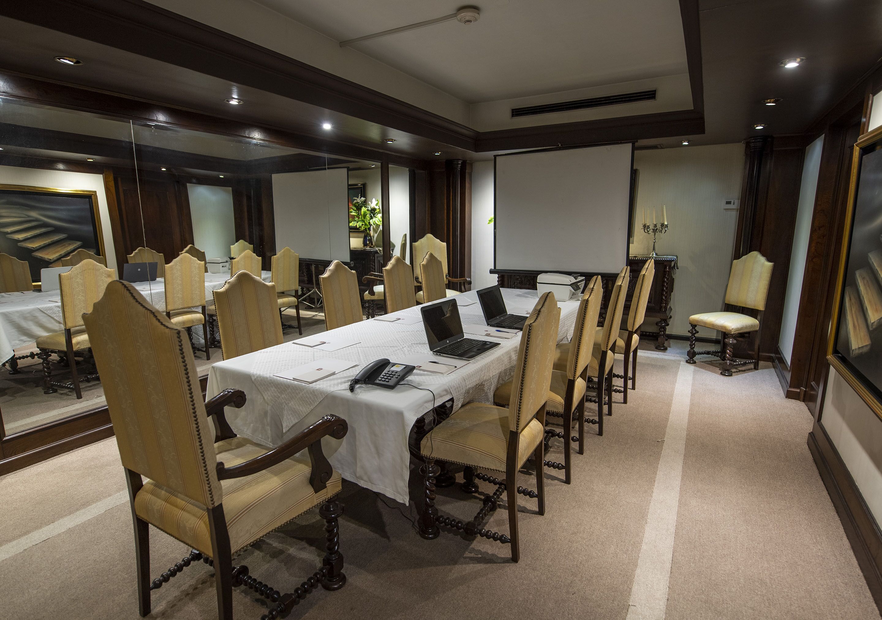A conference room with a long table, multiple chairs, laptops, and a projector screen.