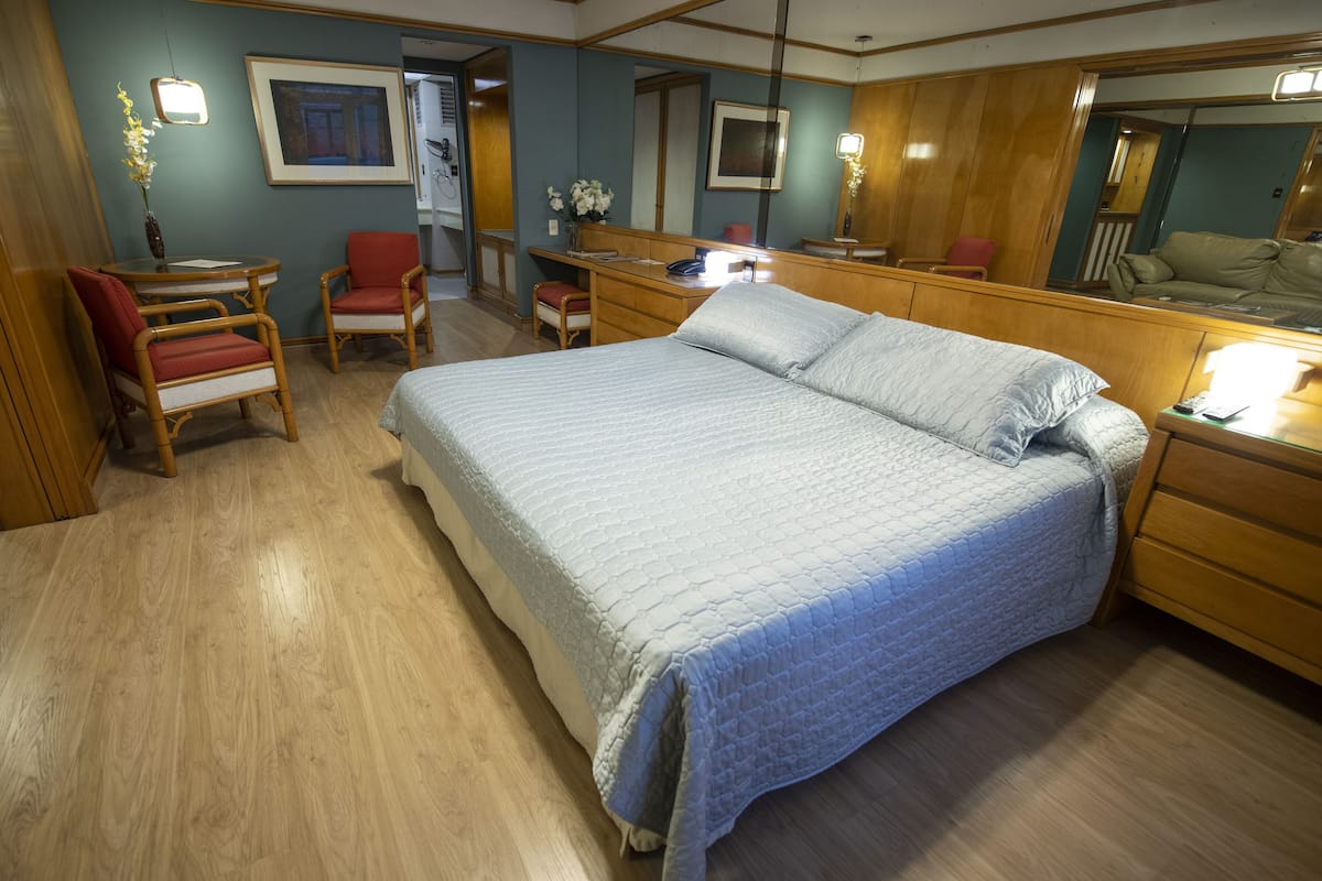 A bedroom with a large bed, a desk, two chairs, a dresser, and a mirror.