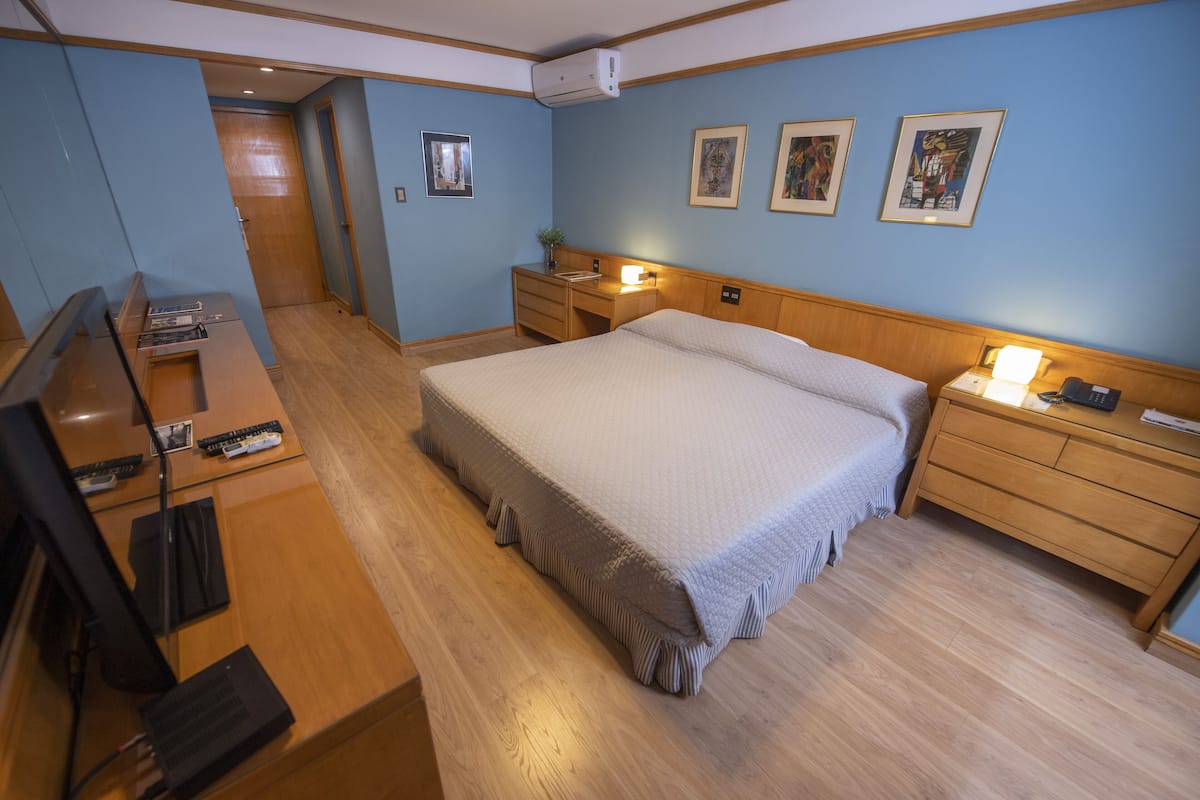A bedroom with a bed, bedside tables, a desk with a computer, and a TV.