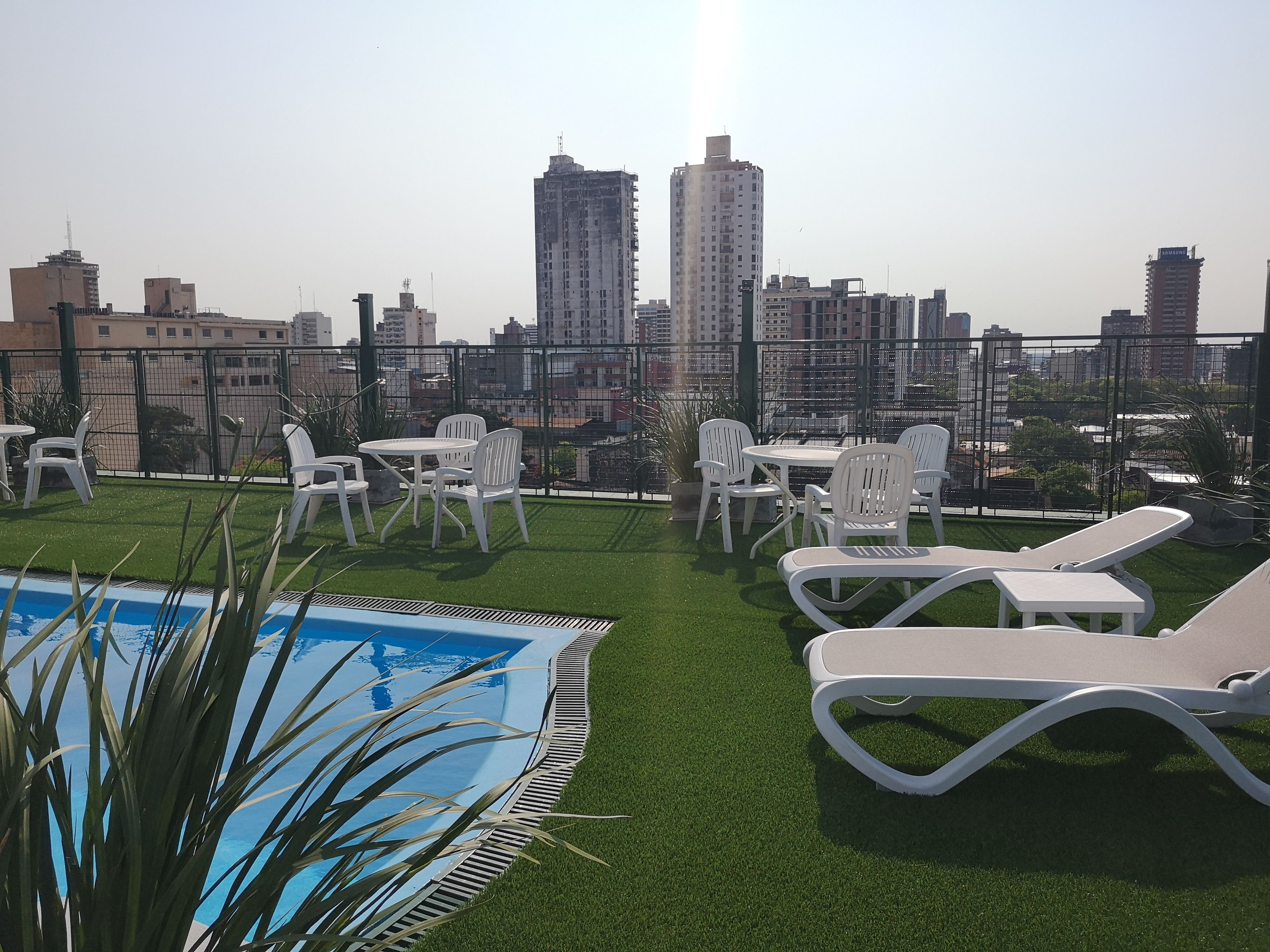 Une terrasse sur le toit avec une piscine, des chaises longues blanches et une table avec des chaises.