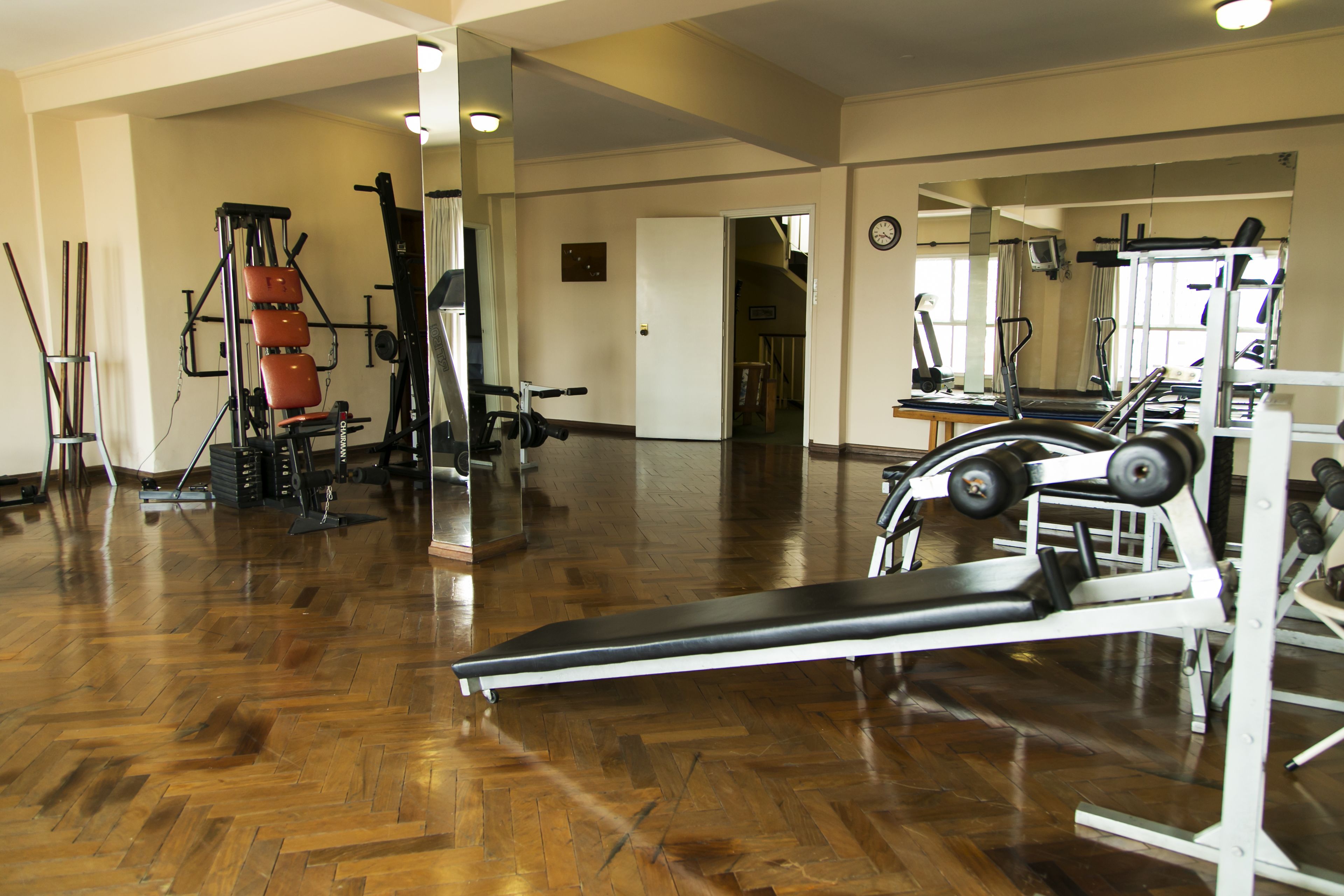 Un gimnasio amplio con diversos equipos de ejercicio, suelo de madera y un espejo grande.
