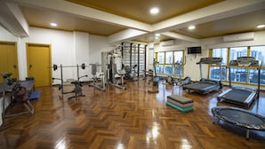 A gym with various exercise equipment, wooden flooring, and large windows offering city views. - Hotel Cecilia (Asunción)