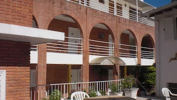 A building with a brick facade, multiple balconies, and outdoor seating with tables and chairs.