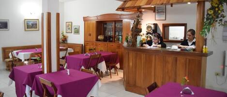 Un restaurante con manteles morados, sillas de madera y una zona de bar con mostrador de madera.