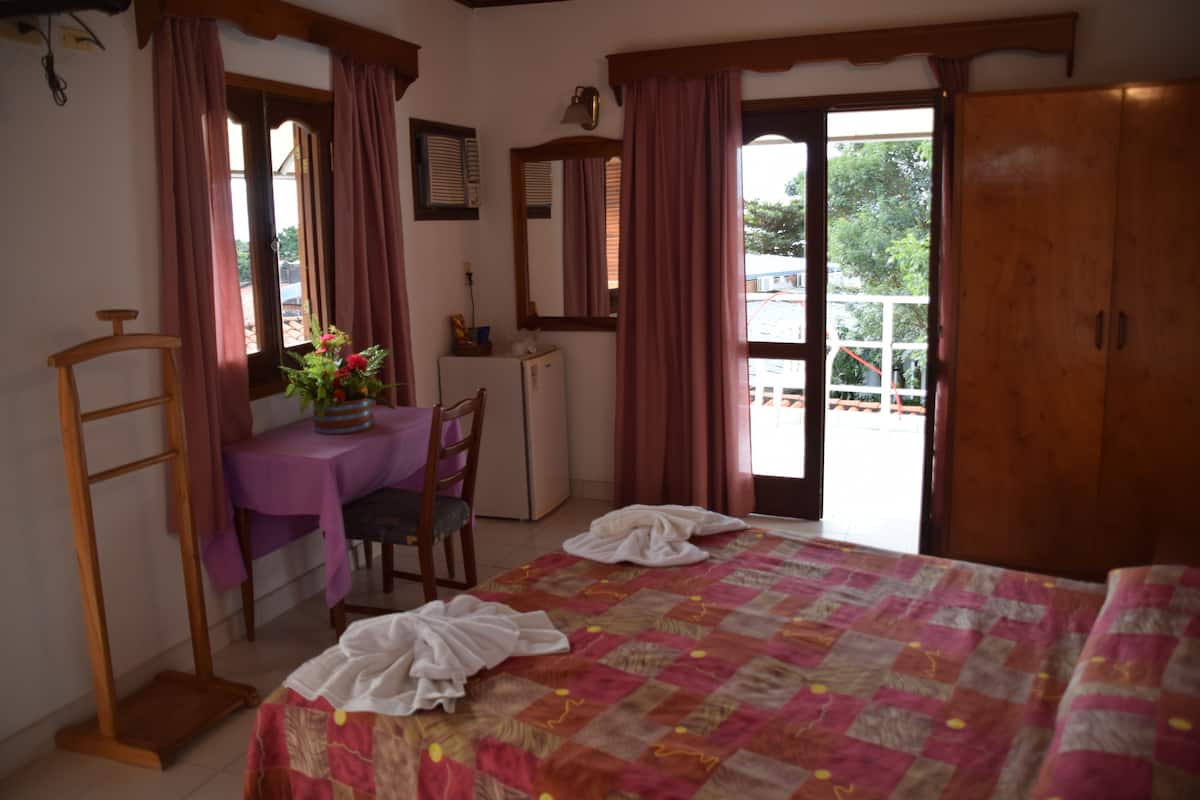 A bedroom with a bed, a desk, a chair, a wardrobe, and a balcony.