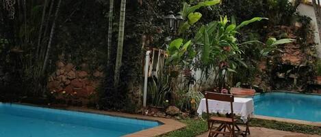 A pool area with lounge chairs and a table, surrounded by lush tropical plants and a stone wall.