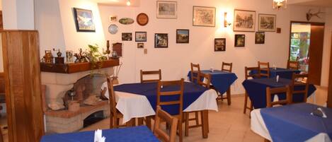 A dining area with tables covered in blue tablecloths, wooden chairs, and a fireplace.