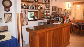 Una zona de bar con mostrador de madera, estantes con botellas, un reloj y un microondas sobre una mesa.