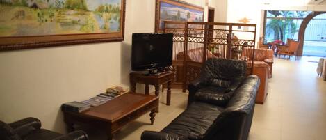 A living room with a leather sofa, a wooden coffee table, a TV, and paintings on the wall.