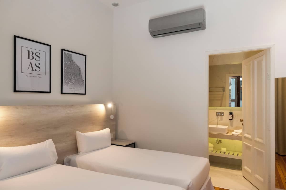 A hotel room with two beds, a headboard, wall-mounted air conditioning, and a bathroom visible through an open door.