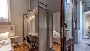 A modern hotel room with a wooden floor, a bed with white linens, a desk with a chair, a large mirror, and a bathroom visible through a glass partition. - Up Tribeca Hotel (Buenos Aires)