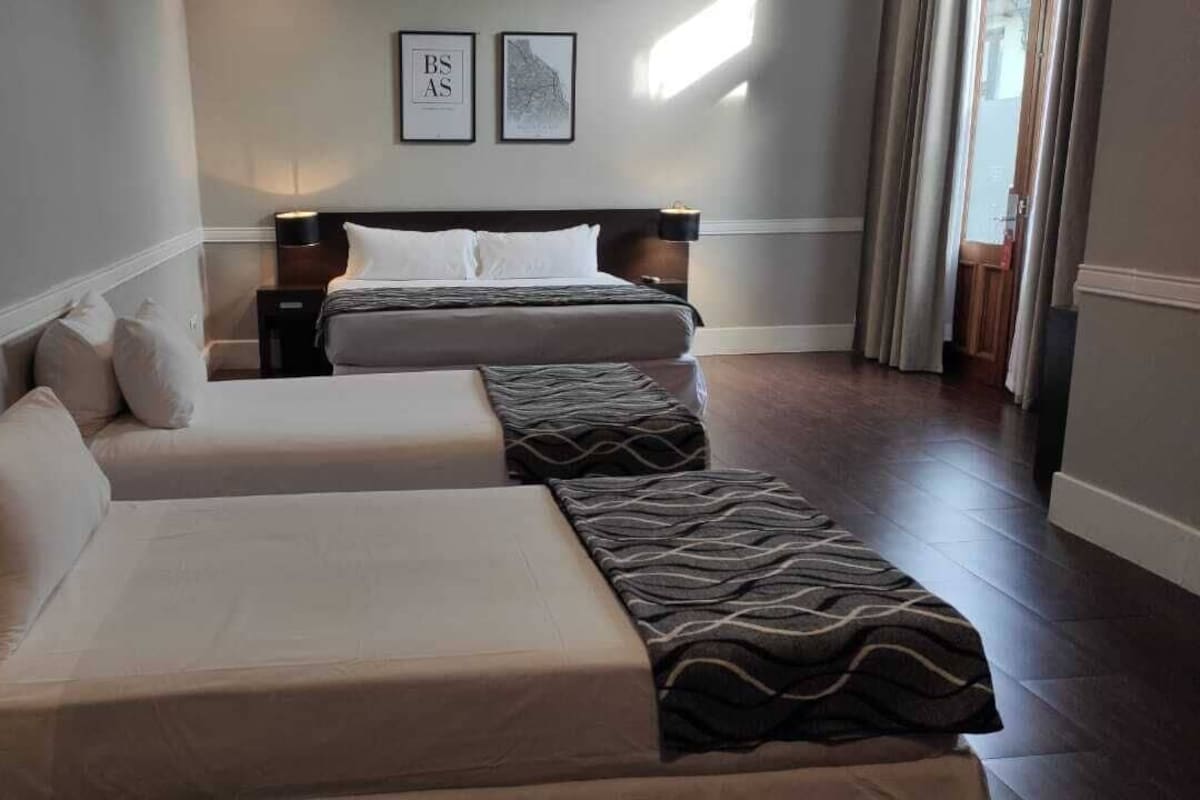 A hotel room with two beds, a sofa, and a nightstand with a lamp.