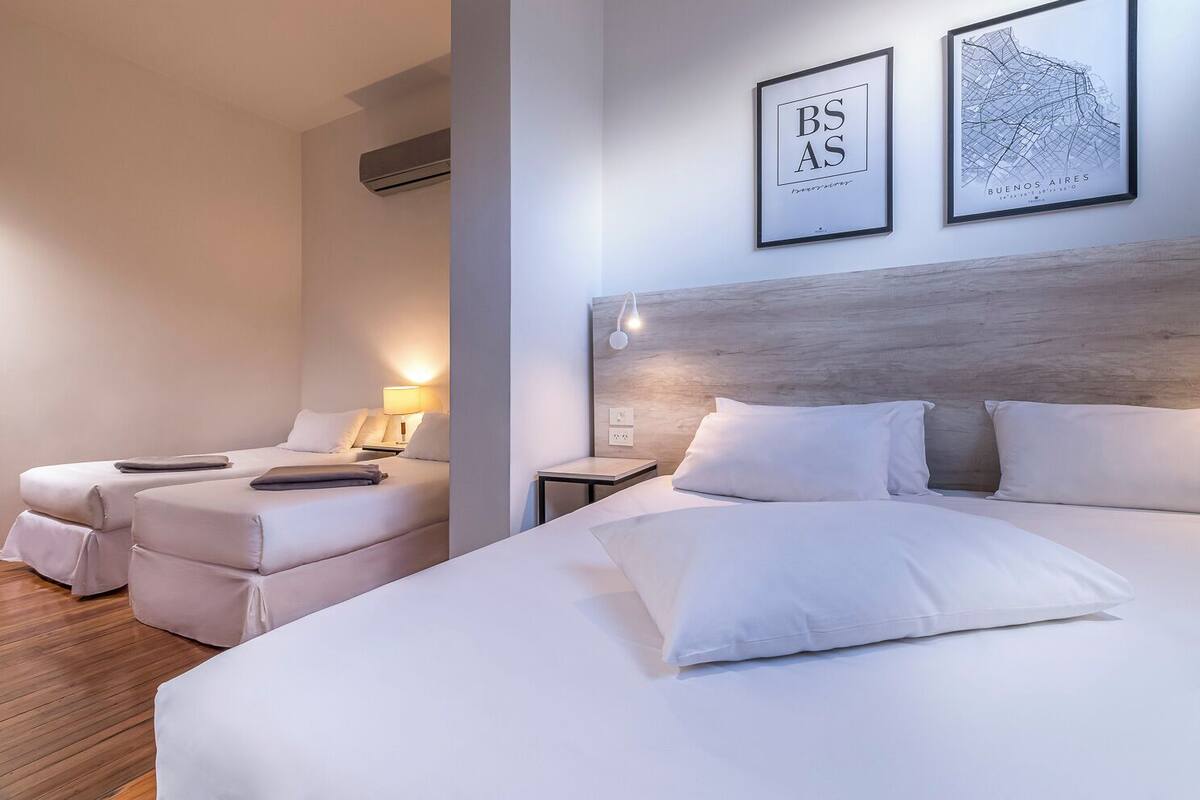 Habitación de hotel con dos camas, cabecero de madera y dos mapas enmarcados en la pared.
