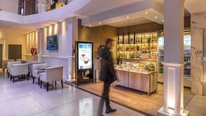 A modern hotel lobby with a seating area, a coffee shop, and a well-lit display of food items. - Up Tribeca Hotel (Buenos Aires)