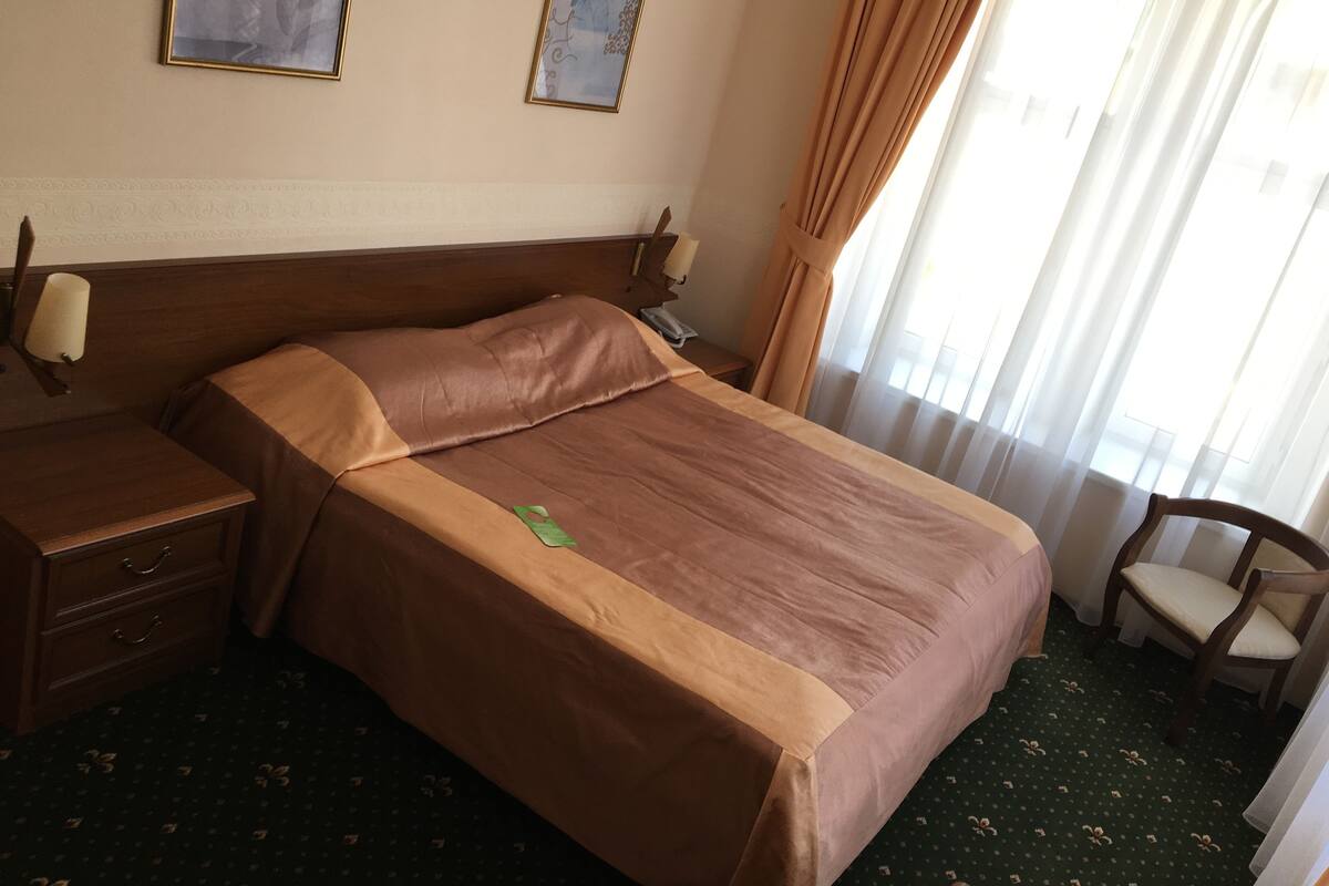 A hotel room with a bed, a nightstand, a lamp, a chair, and a window with curtains.