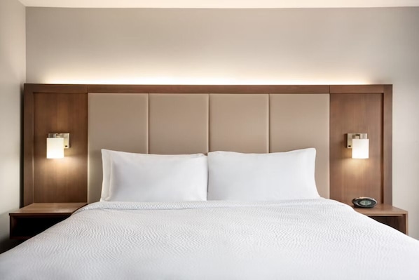 A hotel room with a large bed, two bedside tables, and wall-mounted lighting.