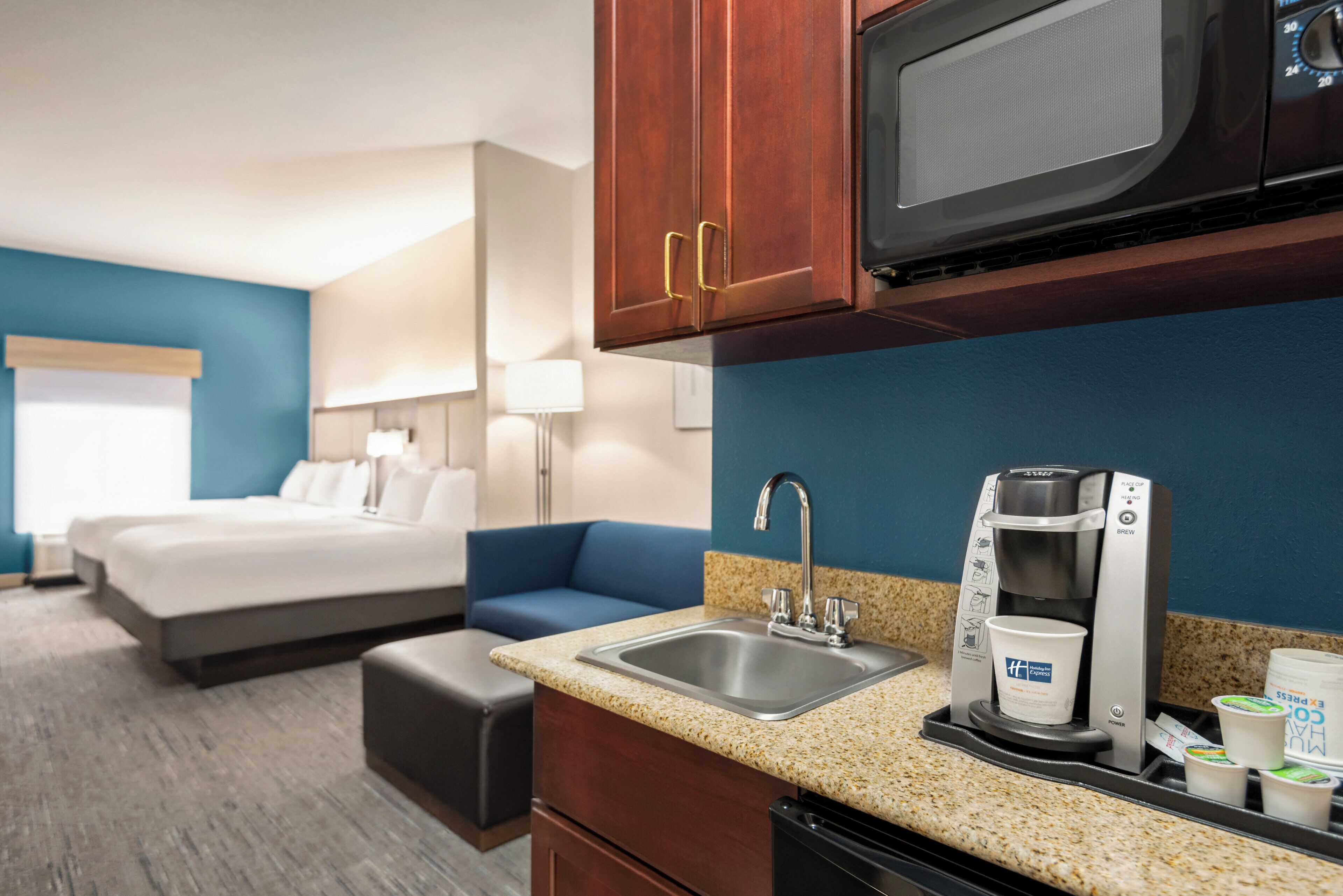 A hotel room with a kitchenette, a bed, a sofa, and a bathroom.