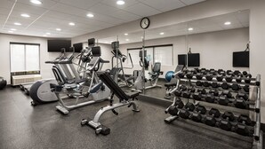 Une salle de sport équipée de matériel d’exercice, avec une horloge et un miroir.