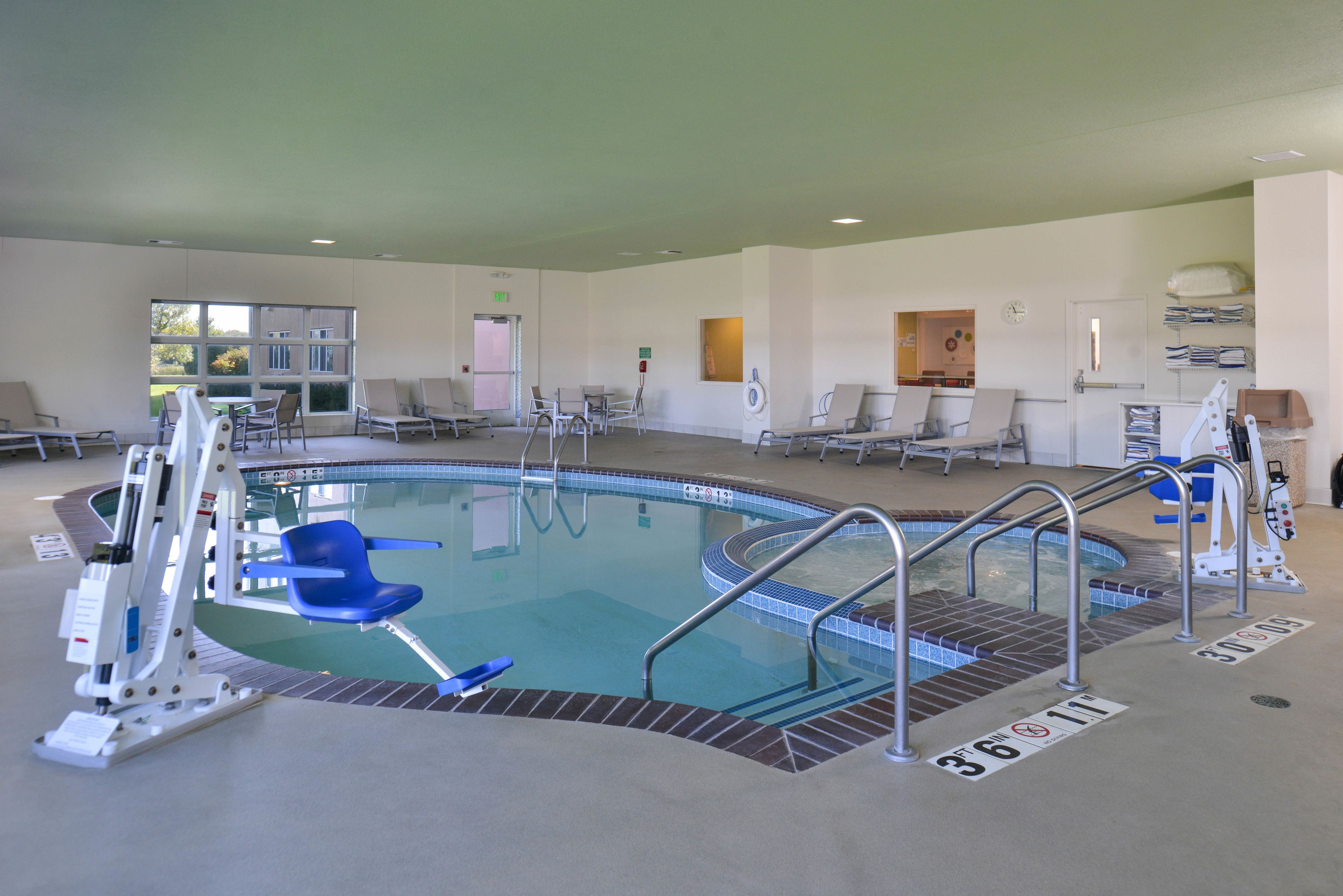 An indoor swimming pool with a clear water surface, surrounded by lounge chairs and a changing room.