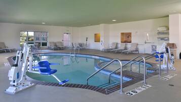 An indoor swimming pool with a clear water surface, surrounded by lounge chairs and a changing room.