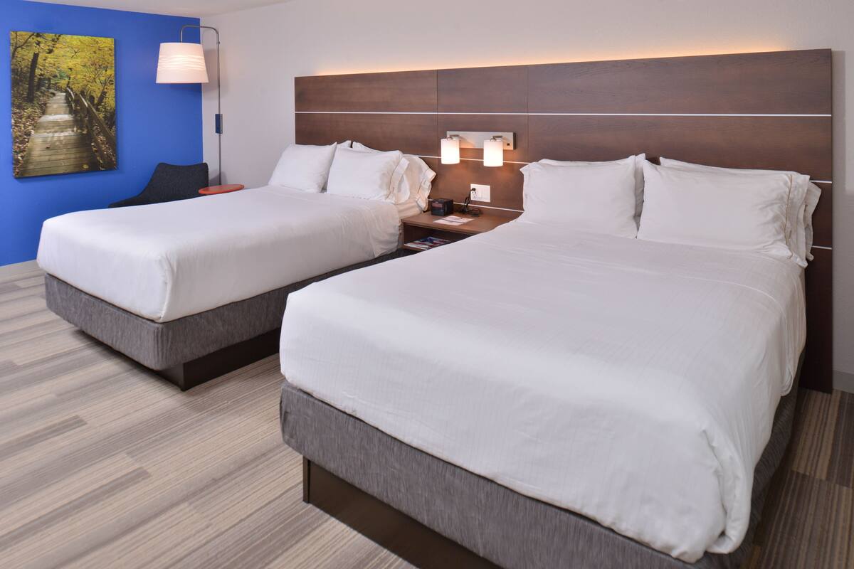 A hotel room with two beds, a nightstand, a lamp, and a painting on the wall.