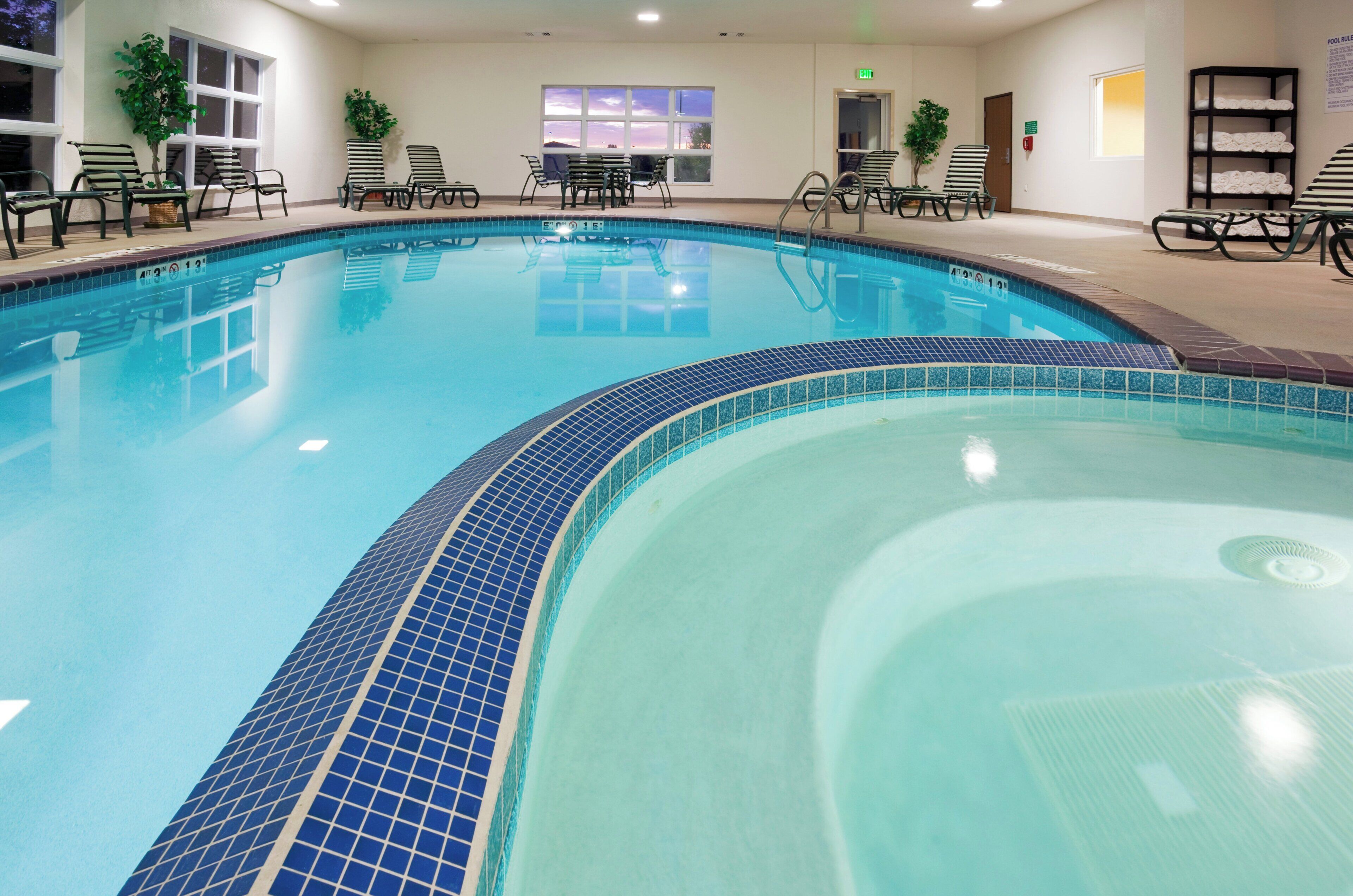 An indoor swimming pool with clear blue water, surrounded by lounge chairs and a tiled deck.